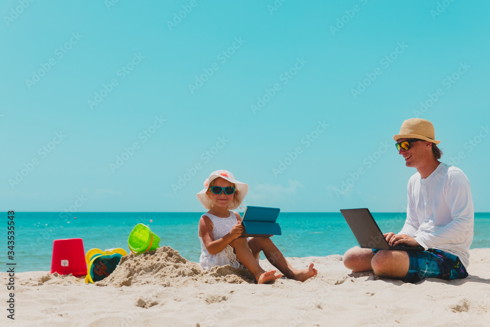 father with laptop and cute daughter with touch pad on beach