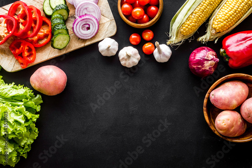 Autumn harvest. Vegetables - potato,cucumber, corn, greenery - frame on black background top-down copy space