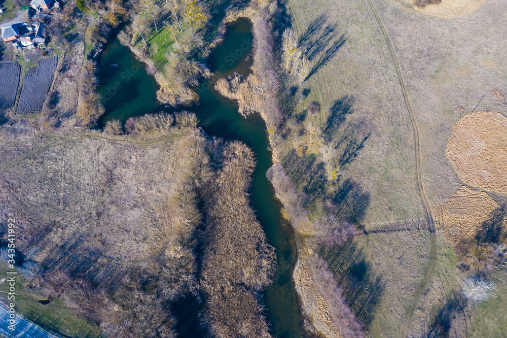 Forest river, beaver dam, treetops, aerial view. European nature at early spring time. Stream, tree crowns, wetland. Aerial landscape.