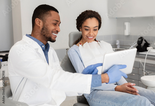 Happy dentist and female patient looking at digital tablet screen