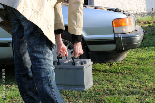 A woman carries a car battery for installation in a car.