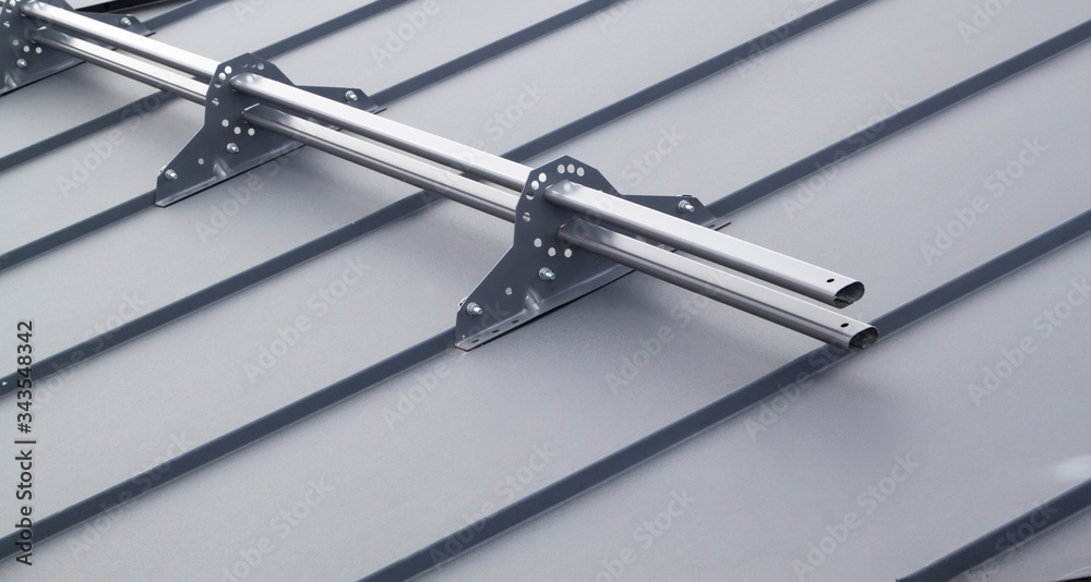 Close up view of fastening metal snow retainer with screws to grey roof Close up view of fastening metal snow retainer with screws to grey roof