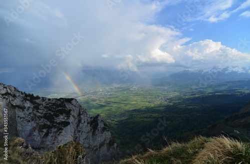 rainbow with rock wall in the foreground and in the background the river Rhine in the valley and the principality of Liechtenstein