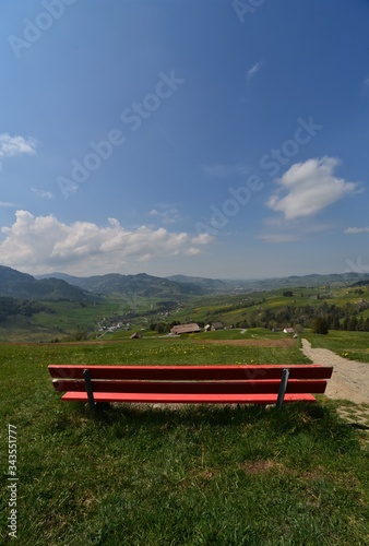 Red bench on a green meadow in Appenzell with a blue sky and clouds