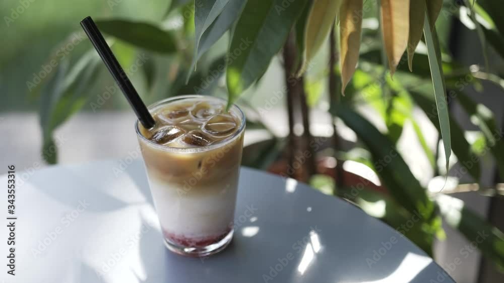 Summer, spring weather. Bright sun. A glass goblet with a straw is on the table. Iced coffee with milk layers. Cold tasty coffee, cocktail with ice. Summer, spring weather. Bright sun. A glass goblet with a straw is on the table. Iced coffee with milk layers. Cold tasty coffee, cocktail with ice.