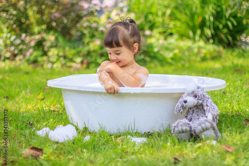 Baby girl bathes in a bathtub in the summer garden