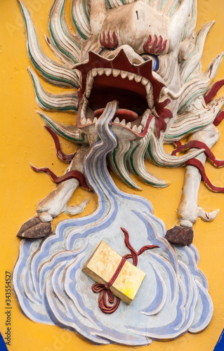 Fengdu, China - May 8, 2010: Yangtze River boat terminal gate. Closeup of head and pool of saliva of beige dragon with violent manes and teeth on yellow backdrop, set in wall.