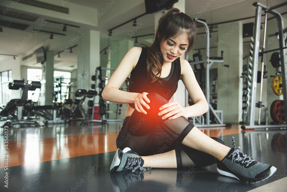 Asian woman injuries during workout at knee in fitness gym sport center. Medical and Healthcare concept. Exercise and Training theme. People healthy lifestyle and leisure activity problem