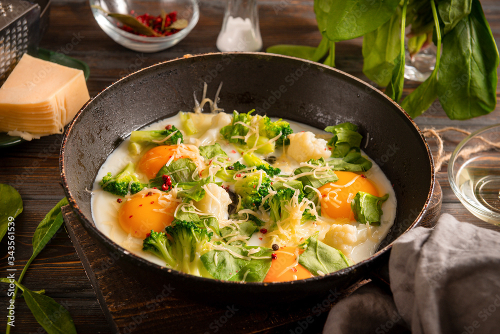 fried eggs with broccoli, spinach, cheese and spices in a pan on a dark wooden background, healthy . Breakfast fried eggs with broccoli, spinach, cheese and spices in a pan on a dark wooden background, healthy . Breakfast