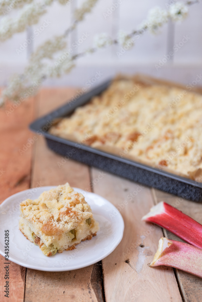Kuchen mit Rhabarber und Streusel aus einem Blech auf einem Tisch aus hellem Holz