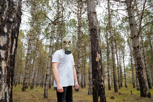 Man in gas mask and white shirt standing in forest. Enviromental protection, ecology, Earth saving, pollution prevention, COVID-19 concept.
