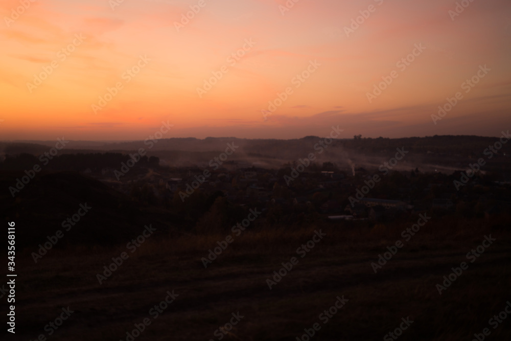 Blurred photo Natural Sunset Sunrise Over Field Or mountains. Bright Dramatic Sky And Dark Ground. Countryside Landscape Under Scenic Colorful Sky At Sunset Dawn Sunrise. Sun Over Skyline Warm Colors.