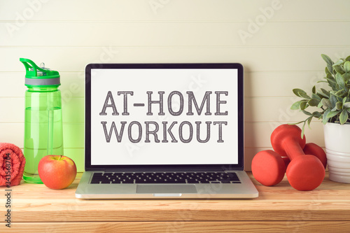 At home workout and healthy lifestyle concept with laptop computer, dumbbels and  plant on wooden table with copy space photo