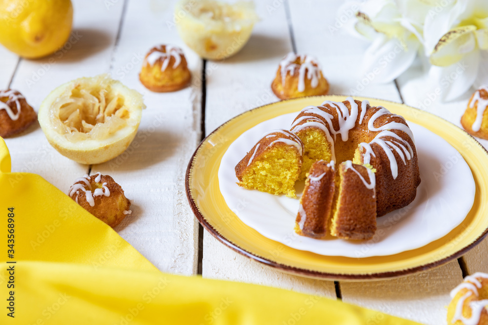 kleiner gelber kuchen bzw gugelhupf aus zitronen mit zuckerguss auf weißem tisch aus brettern und holz kleiner gelber kuchen bzw gugelhupf aus zitronen mit zuckerguss auf weißem tisch aus brettern und holz