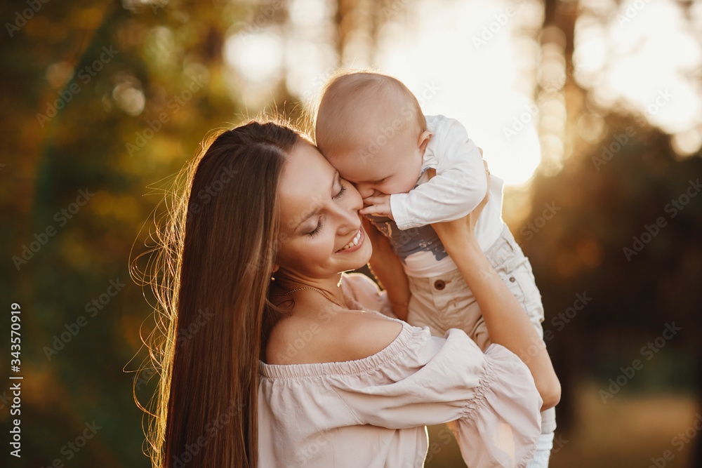 Happy child and his mom have fun outdoors in a field. Mom holds the child in her arms, and the child hugs and kisses the mother. Mother's Day. selective focus Happy child and his mom have fun outdoors in a field. Mom holds the child in her arms, and the child hugs and kisses the mother. Mother's Day. selective focus