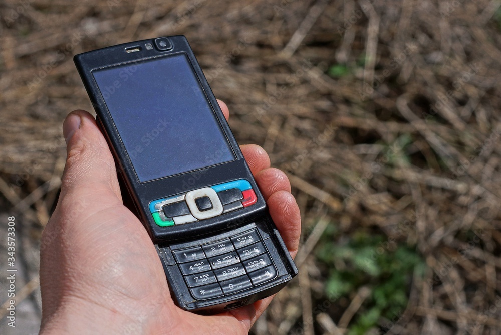 hand holds old black mobile phone outdoors on a sunny day hand holds old black mobile phone outdoors on a sunny day