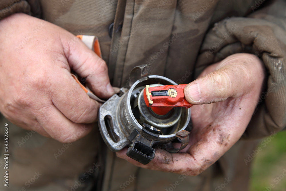 Motor ignition distributor with Hall transducer without cap disassembled from the engine in the hands of a mechanic close-up, car ignition system repair