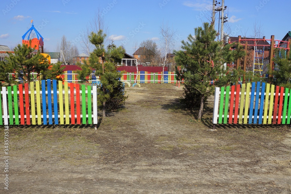 entrance to the playground with green pines and colored wooden decorative fence on the street on a sunny day entrance to the playground with green pines and colored wooden decorative fence on the street on a sunny day
