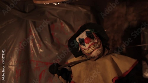 A scarier clown with knife at crude basement with a mirror on the wall