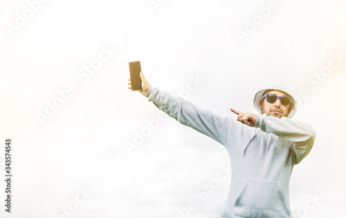 Young man in a grey sweatshirt with blue sunglasses on a white background and pointing at his mobile