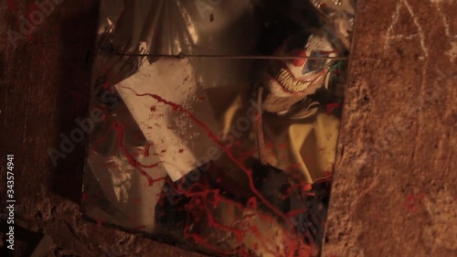A scarier clown with knife at crude basement with a mirror on the wall
