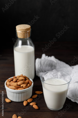 Almond milk in a glass and a glass bottle on dark wooden background