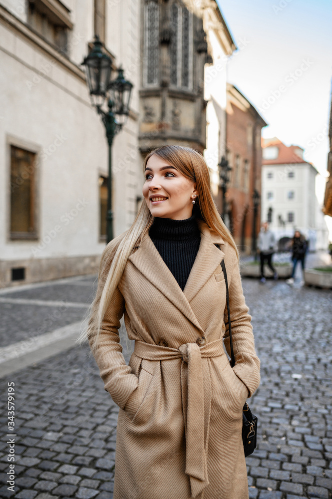 Fototapeta premium Attractive blonde in a beige coat walks around the old town