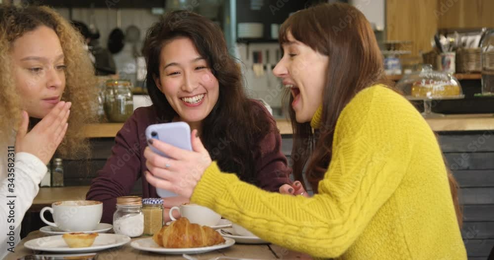 Pan of Woman Showing Her Friends Something Funny On Phone In Cafe Pan of Woman Showing Her Friends Something Funny On Phone In Cafe