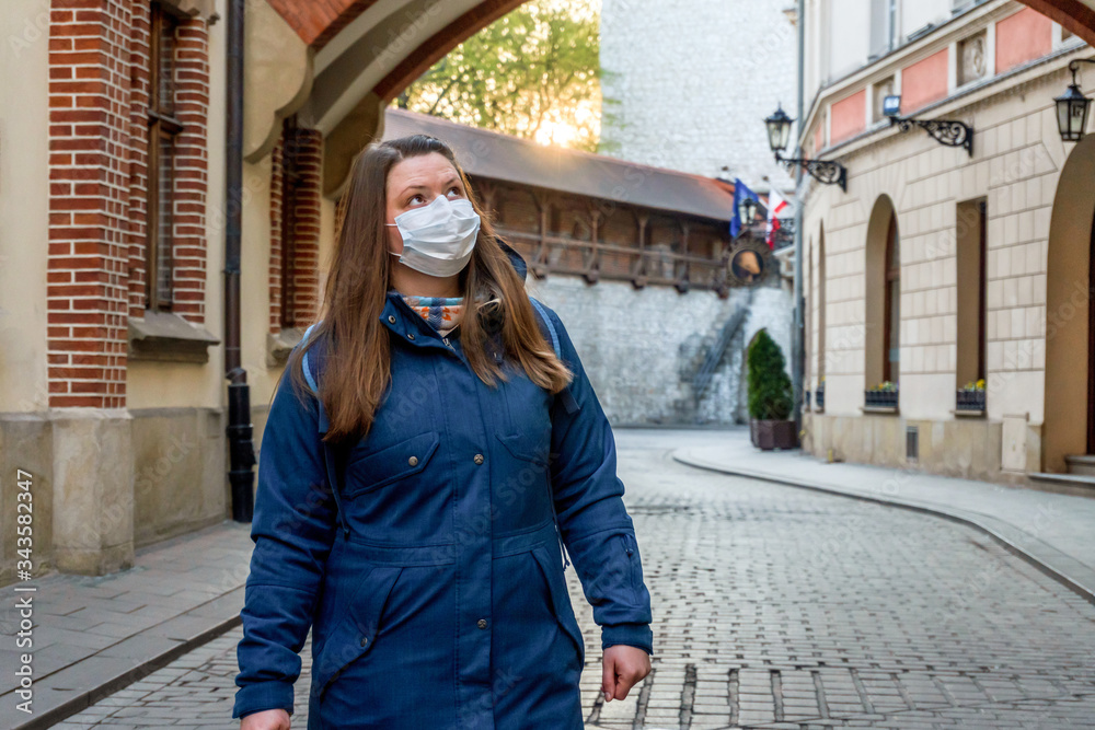 woman in a medical mask walks in empty old city Krakow, Poland. No people or tourists in the city center due to coronavirus infection.