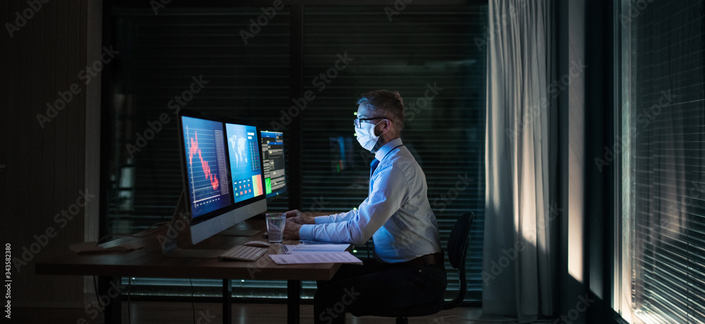 Fototapeta premium Businessman with computer sitting at desk, working late. Financial crisis concept.