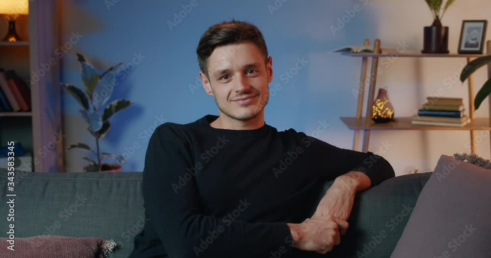 Portrait of happy young guy in black sweater sitting on sofa and possing to camera. Handsome adult man in 30s looking to camera while spending time at home. Concept of people. Portrait of happy young guy in black sweater sitting on sofa and possing to camera. Handsome adult man in 30s looking to camera while spending time at home. Concept of people.