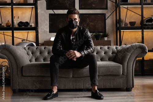 Handsome young manin black mask. Fashionable man in leather jacket standing and looking at window
