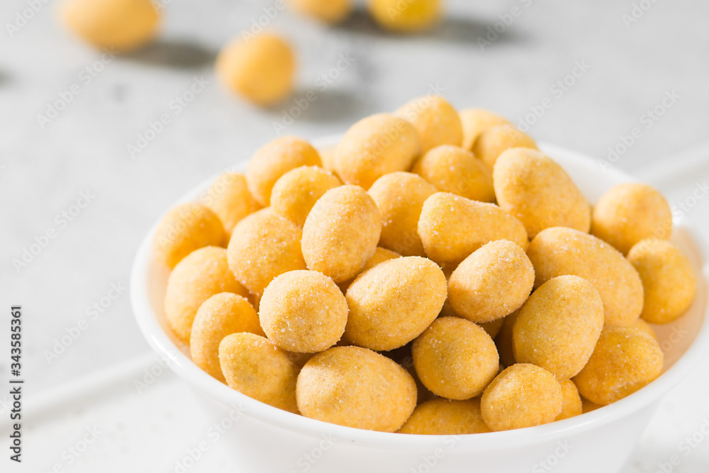Grilled peanuts in cheese sauce in a white bowl on a light gray table. Close-up with space for text Grilled peanuts in cheese sauce in a white bowl on a light gray table. Close-up with space for text