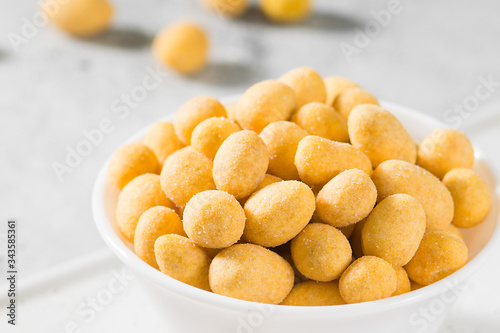 Grilled peanuts in cheese sauce in a white bowl on a light gray table. Close-up with space for text