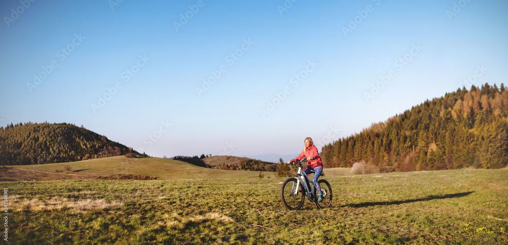 Fototapeta premium Active senior woman with e-bike cycling outdoors in nature.