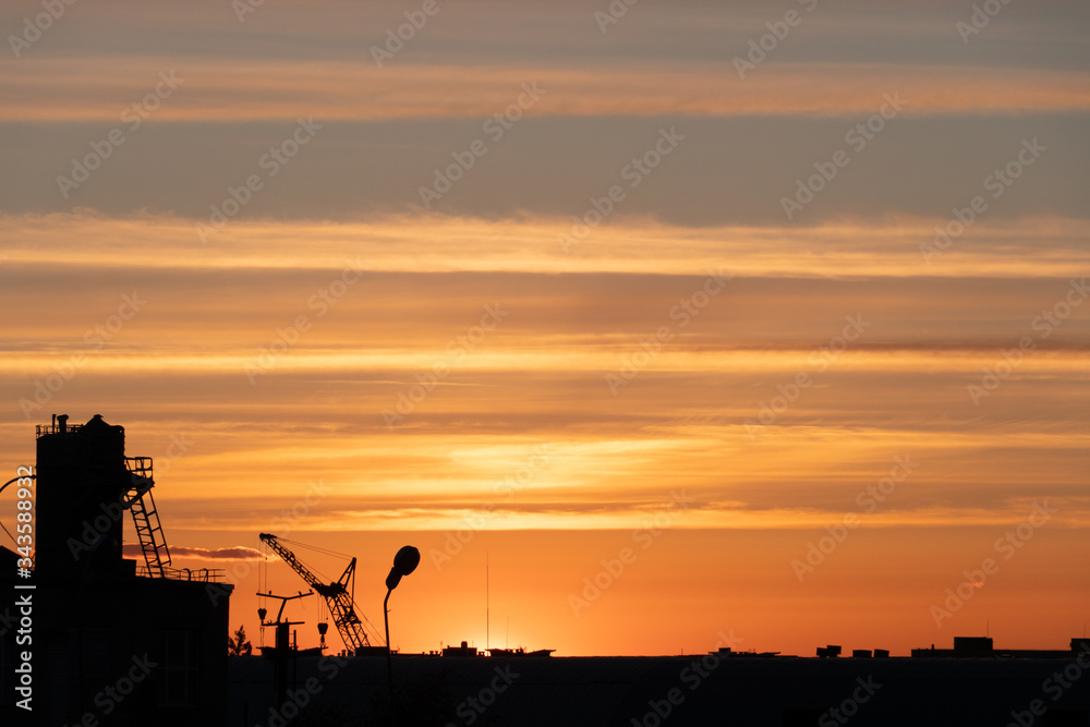 Evening outline of the city. The silhouette of the factory against the sky or sunset. The tower crane operates on the territory of the factory. Evening outline of the city. The silhouette of the factory against the sky or sunset. The tower crane operates on the territory of the factory.