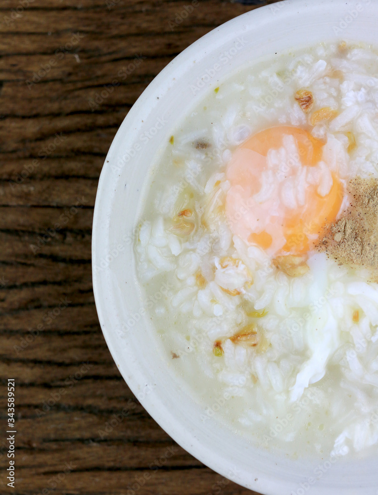 Homemade Thai Rice Soup With chicken, pork and Soft boiled egg or onsen egg in white blow on rustic wooden background. Thai style Food. Top view. Homemade Thai Rice Soup With chicken, pork and Soft boiled egg or onsen egg in white blow on rustic wooden background. Thai style Food. Top view.