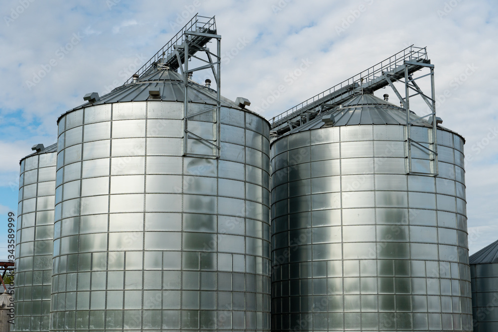 silver silos on agro manufacturing plant for processing drying cleaning and storage of agricultural products, flour, cereals and grain. Large iron barrels of grain. Granary elevator silver silos on agro manufacturing plant for processing drying cleaning and storage of agricultural products, flour, cereals and grain. Large iron barrels of grain. Granary elevator