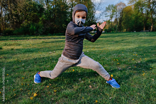 Kid boy wearing like ninja does different exercises outdoor