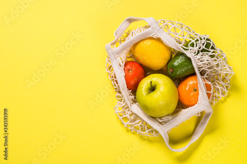 Mesh bag with fruits on color background.