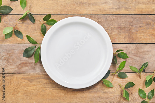 Empty white plate with green leaf on wooden table. Top view.
