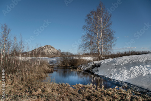 Spring landscape of Bashkortostan. A lonely mountain, a shihan, around a plain, rare trees and snow in gullies.