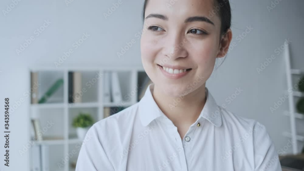 A charming happy young asian businesswoman is looking and smiling to the camera while sitting in the white office A charming happy young asian businesswoman is looking and smiling to the camera while sitting in the white office