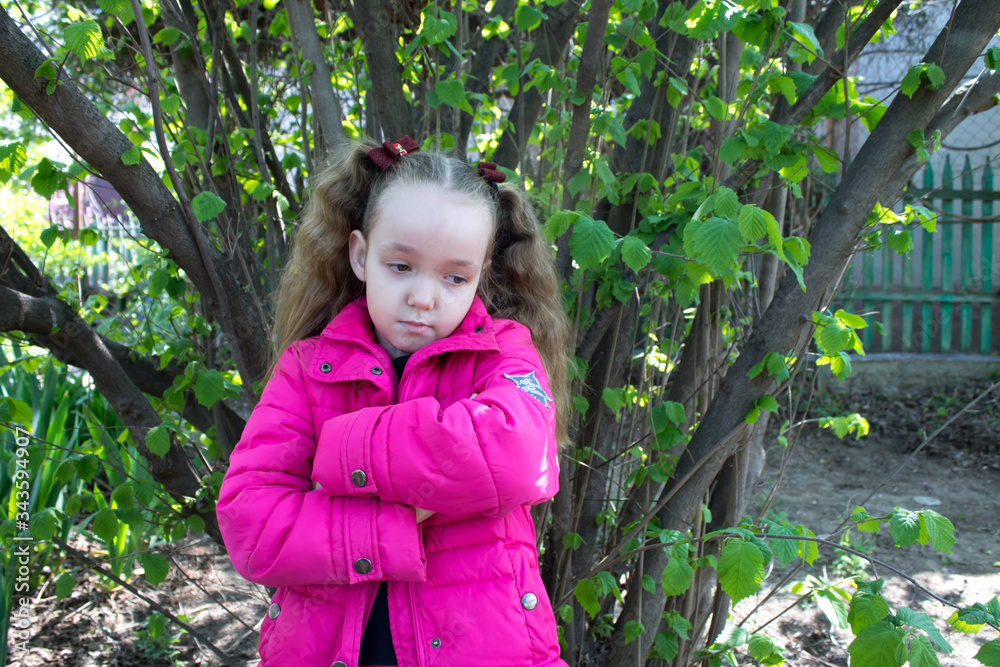 little girl in a pink jacket is sad in the spring in the garden near the house