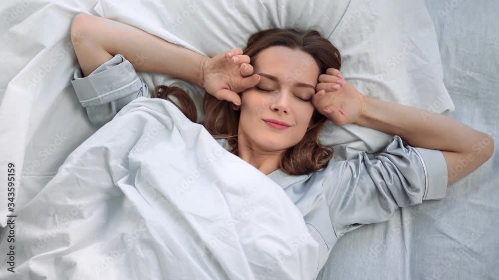 Top view portrait of young awakening woman stretching on bed. Medium close up shot on 4k RED camera