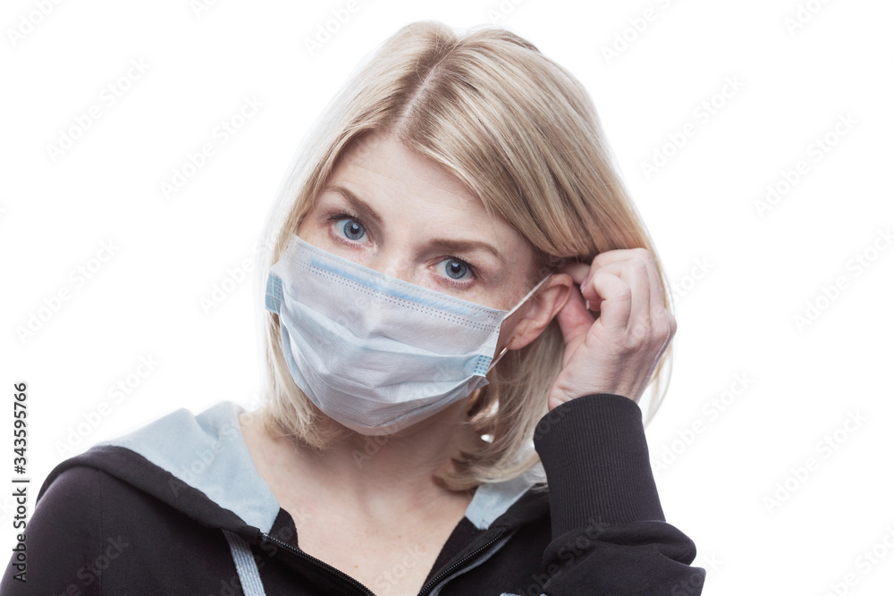 Blonde woman puts on a medical mask. Precautions during seasonal allergies. Self-isolation mode in the coronavirus pandemic. Close-up.Isolated on a white background. Blonde woman puts on a medical mask. Precautions during seasonal allergies. Self-isolation mode in the coronavirus pandemic. Close-up.Isolated on a white background.