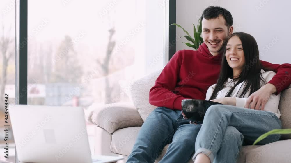 The boyfriend and girlfriend are at home watching films. The couple is eating popcorn and smiling. The boyfriend and girlfriend are at home watching films. The couple is eating popcorn and smiling.