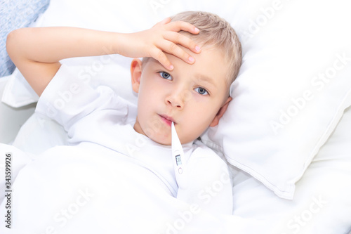 boy lies in bed with a thermometer in his mouth. healthcare concept and sick child, coronavirus, high fever,