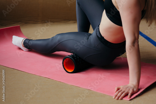 Close-up An athletic Pilates trainer does exercises with a massage cylinder on a yoga mat. photo