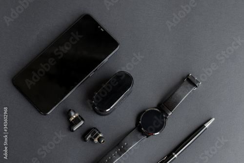 Accessories for men's beauty on a monochromatic background. black pen, black smart watch, smartphone and wireless headphones on dark background. View from above. Minimalist black trend 2020.